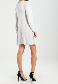 Abito grigio a maniche lunghe con scollatura rotonda e orlo svasato, abbinato a scarpe con tacco alto nere e strappy, fotografato da dietro.