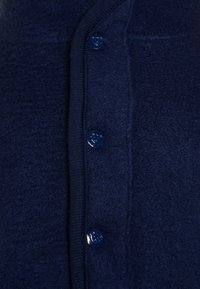 Suéter de lana azul marino con una textura suave, ribeteado en la orilla y botones brillantes. Los botones están colocados a lo largo de la abertura frontal.