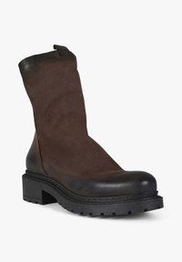 Stivaletto alla caviglia in camoscio marrone con punta in pelle nera liscia e suola in gomma robusta. Presenta un design minimale con un tacco leggermente rialzato.