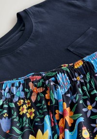 Marineblaue Hemd mit Brusttasche, kombiniert mit schwarzen Hose mit elastischem Bund, die bunte Blumen- und Vogelmuster aufweist und einen Kordelzug hat.