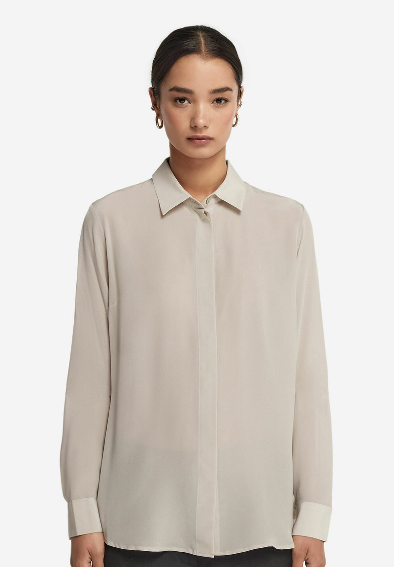 Beige Bluse mit langen Ärmeln, aus leichtem Stoff, mit Standardkragen, geknöpftem Vorderteil und Manschetten. Glatte Textur mit lockerer Passform.