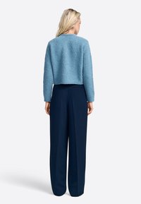 Pull cropped bleu clair et moelleux à manches longues associé à un pantalon navy taille haute et large. Design minimaliste sans motifs.