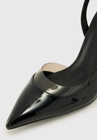 Scarpa con tacco alto in vernice nera, dal punta affusolata e con un accento trasparente sulla parte superiore. Superficie liscia con linee eleganti.