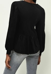 Schwarze Peplum-Bluse mit Puffärmeln und Rundhalsausschnitt; aus strukturiertem Stoff gefertigt, mit gerafftem Taillenbereich und glattem Saum.