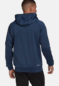 Sudadera con capucha azul marino hecha de tejido suave; cuenta con un bolsillo tipo canguro y puños de canalé. Etiqueta situada en el dobladillo inferior.