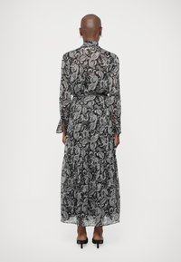 Μαύρο και άσπρο μακριά φορεσιά με σχέδιο paisley από διαφανές ύφασμα, με φαρδιά τέρματα και μακριά μανίκια. Διαθέτει δέσιμο στη μέση και διακριτικούς καμπυλωτούς μανίκες.