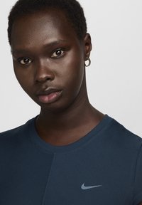T-shirt sportivo navy con texture a coste, scollo rotondo e logo Nike di colore azzurro chiaro. Il modello indossa un piccolo orecchino ad anello dorato.