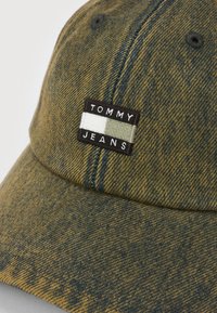 Džinsinio audinio beisbolo kepuraitė išblukusios žalios spalvos, su siuvinėtu Tommy Jeans logotipo pleistru, kuriame yra baltos ir alyvuogių spalvų blokai.