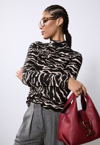 Haut à col roulé rayé noir et beige, associé à un pantalon gris en pied-de-poule. Tient un sac à main bordeaux texturé avec des accessoires dorés.