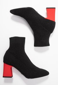 Botas negras hasta el tobillo con un exterior de lana texturada, cuello acanalado y un tacón cuadrado con un acento rojo en la base.