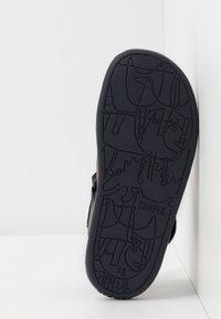 Czarna gumowa podeszwa buta z tłoczonymi wzorami zwierząt i nazwą marki "CAMPER". Bok buta wykonany jest z brązowego materiału i posiada regulowany pasek.