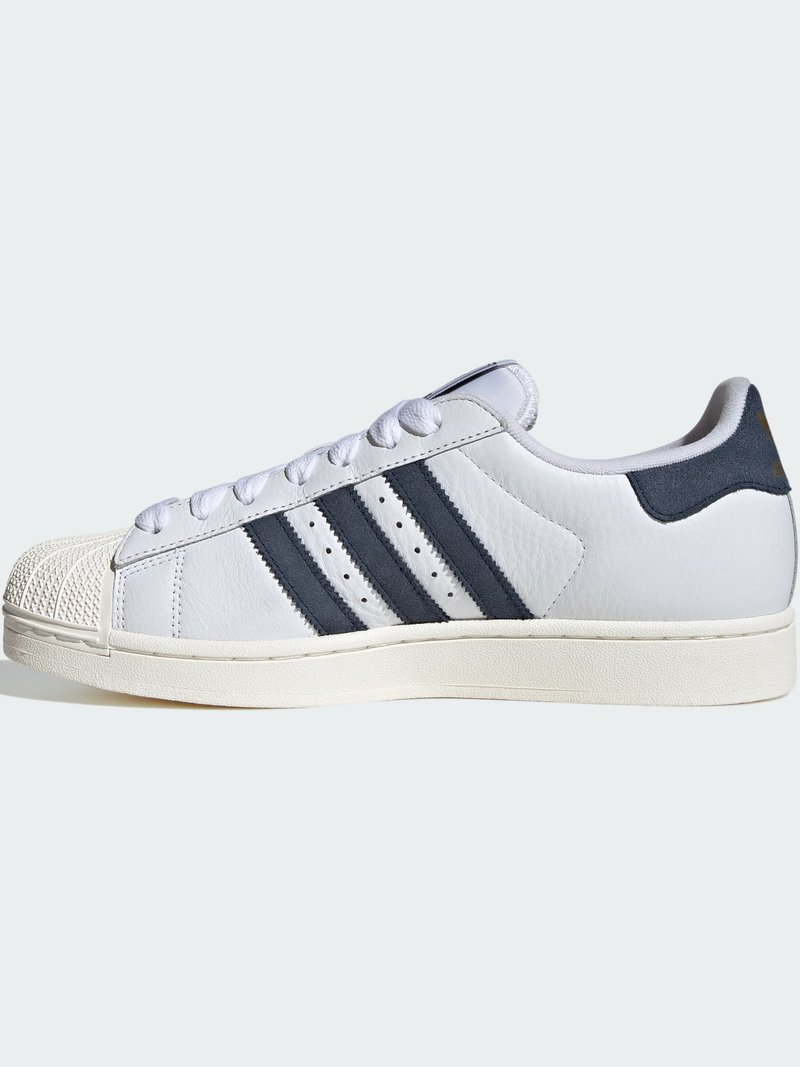White low-top sneaker with black stripes, shell toe, white laces, and cushioned sole, viewed from the outside side.