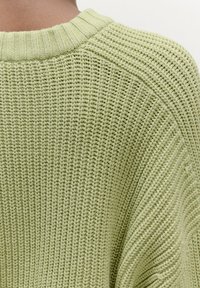 Limegrüner gestrickter Pullover mit geripptem Muster, überschnittenen Schultern und einem Rundhalsausschnitt, der eine lockere, entspannte Passform zeigt.