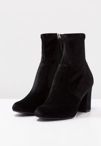 Bottines en velours noir avec bout arrondi, fermeture éclair latérale et talon chunky, présentant une texture lisse et un design élégant.