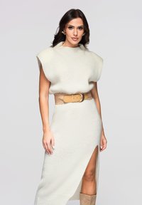 Robe en maille beige clair avec des manches courtes structurées et une fente latérale. Taille cintrée avec une ceinture marron ornée d'une grande boucle circulaire.