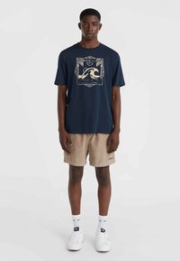 Navy cotton t-shirt with a cream wave graphic and palm tree design, paired with beige corduroy shorts and white sneakers.