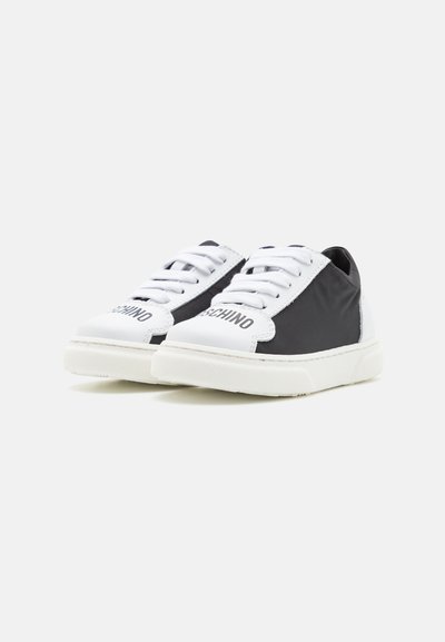 Zapatillas con parte superior de tejido negro y suela de goma blanca, con cordones blancos y logotipo en el lateral. Textura suave y diseño minimalista.
