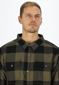 Black and olive green plaid shirt with a collared neck, two front pockets, and snap button closure. Fabric has a smooth texture.