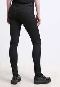Černé skinny džíny vyrobené z denimu, s vysokým pasem a zadními kapsami. V kombinaci s černými botami, které podtrhují štíhlou siluetu.