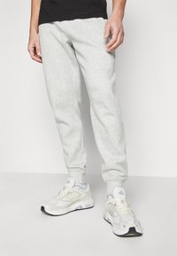 Pantalones de chándal gris claro con puños elásticos, hechos de tela suave. Combinados con zapatillas de running blancas con un diseño texturizado y tres rayas.