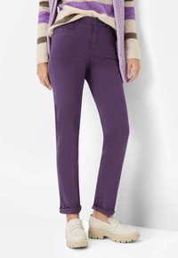 Paarse broek van katoenmix met opgerolde pijpen, gecombineerd met beige loafers met een gestructureerde zool. Witte achtergrond.