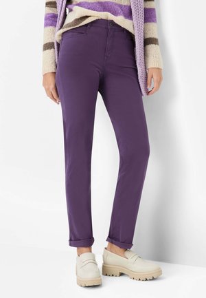 Lilla bomuldsblandede bukser med opbukte manchetter, parret med beige loafers med en struktureret sål. Baggrunden er ren hvid.