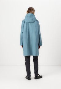 Light blue, hooded coat with a loose fit, long sleeves, and side slits; worn over dark gray pants and black shoes.