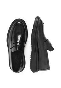 Mocasines negros brillantes con una suela gruesa y texturizada, que presentan una correa sobre el empeine. Acabado suave y sin detalles de hardware visibles.