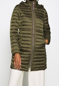 Giacca puffer verde oliva con trapuntatura orizzontale, chiusura con zip, cappuccio e tasche laterali. Il tessuto appare liscio e lucido, con polsini elasticizzati.
