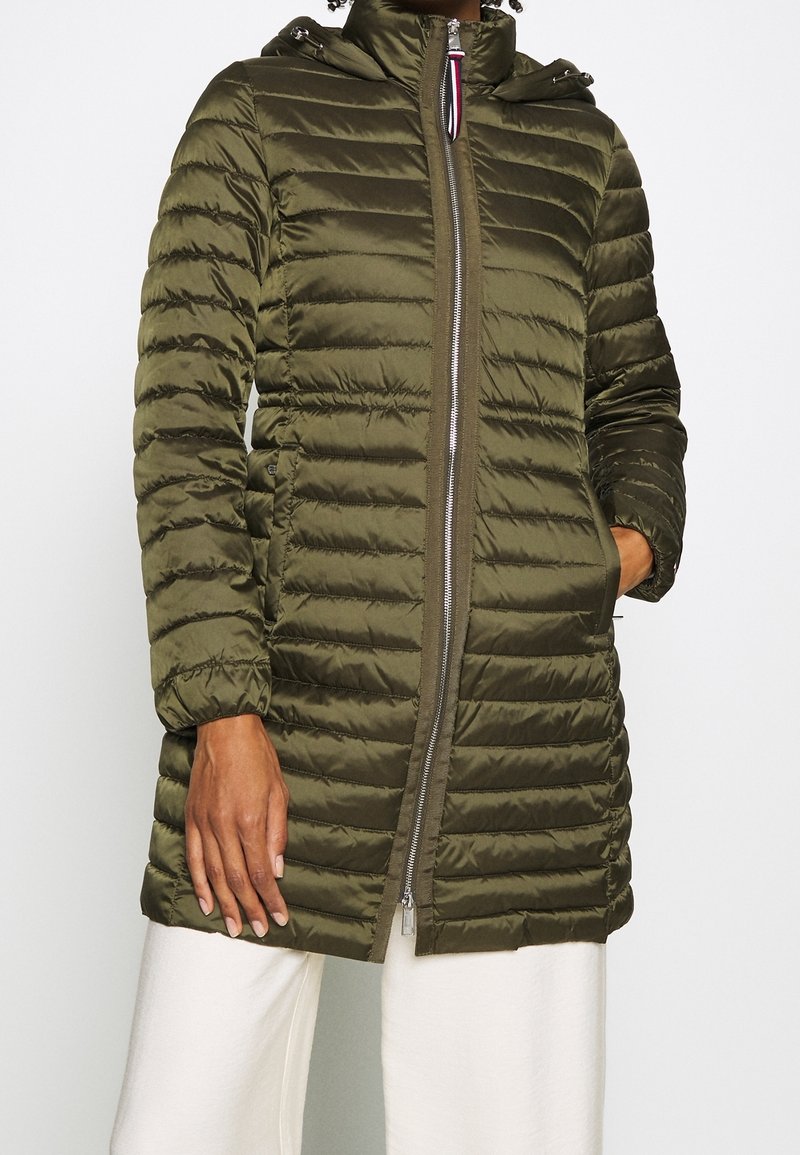 Giacca puffer verde oliva con trapuntatura orizzontale, chiusura con zip, cappuccio e tasche laterali. Il tessuto appare liscio e lucido, con polsini elasticizzati.
