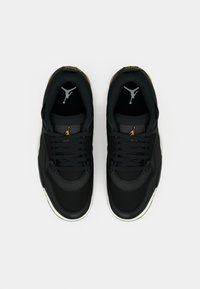 Must-valged mustad ja valge Air Jordani kingad kuldsete Jumpman-logo'dega, vaadatud ülalt lihtsal heledal taustal.