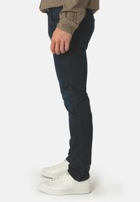 Mörkblå skinny jeans med en mjuk textur, som har en nära passform och subtila sömdetaljer, tillsammans med vita låga sneakers.