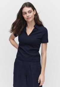 Laivastokuvioinen lyhythihainen polo-paita, jossa on teksturoitu kuosi ja V-pääntie. Yhdistetty tummiin housuihin, jotka korostavat istuvuutta.