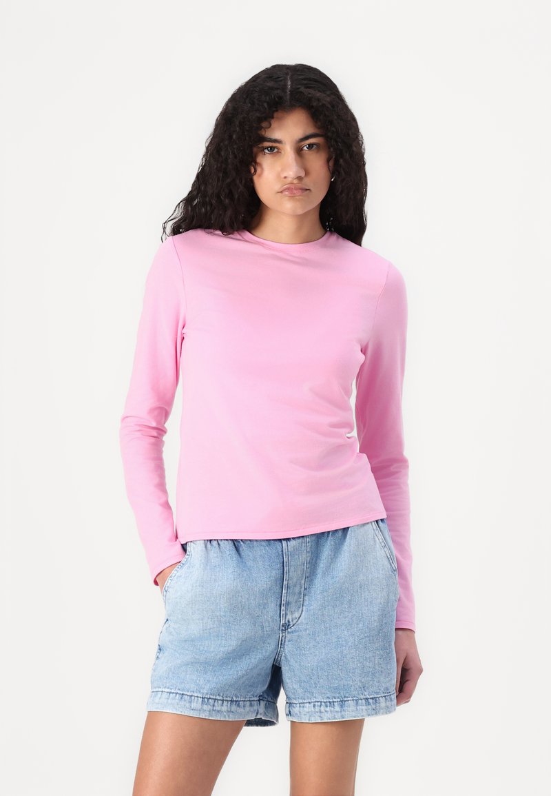 Langarm-Pinkshirt mit Rundhalsausschnitt, aus weichem Stoff gefertigt. Kombiniert mit hellblauen Denim-Shorts mit elastischem Bund.