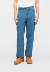 Jeans de ganga azul claro com um corte confortável, cinco bolsos e costuras subtis. Combinados com botas bege com atacadores dourados.