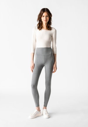 Leggings grigi con vita alta, realizzati in un materiale morbido e elasticizzato. Abbinati a un top aderente a maniche lunghe chiaro e sneakers bianche.