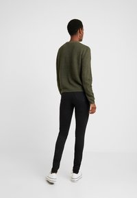 Grön texturerad stickad tröja, åtsittande svarta jeans och vita sneakers. Tröjan har rund hals, långa ärmar och ribbad detalj.