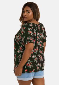 Blommig topp i svart tyg med röda och vita blommor. Har puffärmar och en lös passform, tillsammans med ljusa denimshorts.