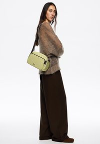 Light green shoulder bag with black accents, rectangular shape, and dual zip closures. Finished with a detachable strap.