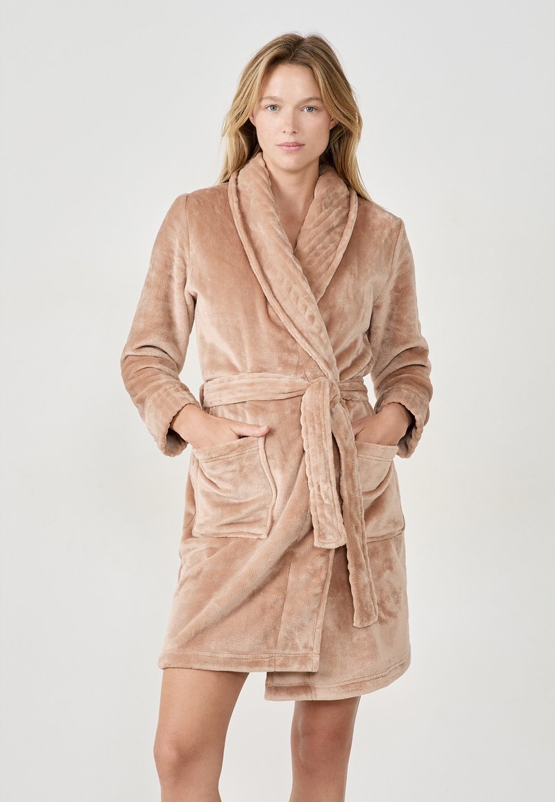 Accappatoio corto in peluche color beige chiaro, con colletto sciallato, vita con cintura e due tasche anteriori. Il tessuto è morbido e con una texture piacevole.