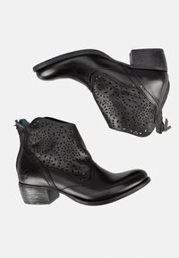 Botas de tobillo de cuero negro con diseño perforado, puntera redonda y tacón bajo. Presentan una cremallera lateral para facilitar el uso.