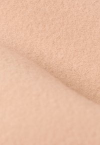 Tissu beige doux avec une surface texturée et légèrement duveteuse, présenté en gros plan avec des plis superposés.