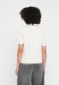 Polo de manga corta en color crema con cuello y puños acanalados, con rayas negras. La tela parece suave con una textura lisa.