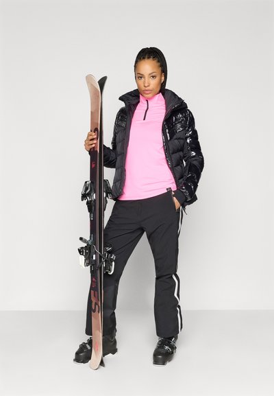 Μαύρο παλτό με αφρώδη υφή και γυαλιστερή επιφάνεια, ροζ μπλούζα με μακριά μανίκια, μαύρο παντελόνι με λευκές ρίγες, μπότες σκι και σκι με δέστρες.