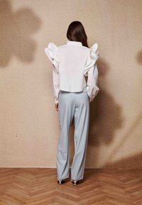 Λευκό πουκάμισο με λεπτομέρειες βολάν στους ώμους, συνδυασμένο με ανοιχτό μπλε παντελόνι. Ομαλές υφές, εφαρμοστή σχεδίαση και παπούτσια με τακούνι ολοκληρώνουν το σύνολο.