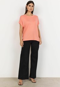 Haut corail à manches courtes avec un col rond, associé à un pantalon large noir. Le haut présente une texture lisse et une coupe décontractée.