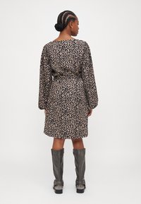 Haljina s leopard-print uzorkom u bež i crnoj boji, s dugim rukavima, opuštenim krojem i okruglim izrezom, uparena sa sivim čizmama do koljena.