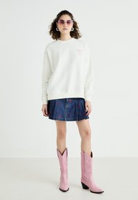 Witte sweatshirt met roze logo, spijkerrok met rode geborduurde details en roze cowboylaarzen met een puntige neus en gestikte design.