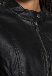 Black leather jacket featuring a high collar, an asymmetrical zipper, and textured surface with visible stitching details.