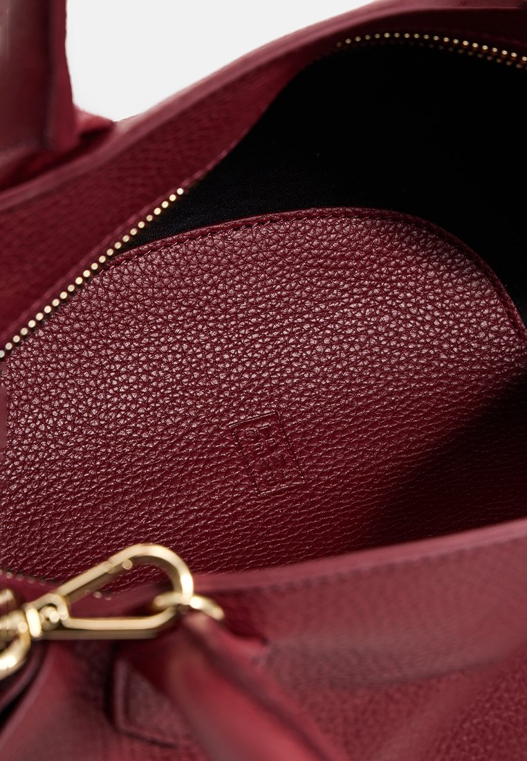 Interno di una borsa in pelle borgogna, superficie testurizzata, dettaglio della zip dorata e fodera scura, che mette in mostra un design spazioso.